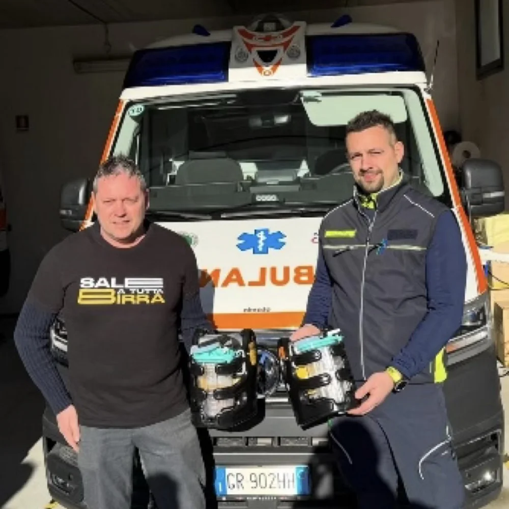 Due uomini in posa davanti all'ambulanza: uno con la maglia di Sale a tutta birra e un volontario tengono insieme due aspiratori portatili appena donati