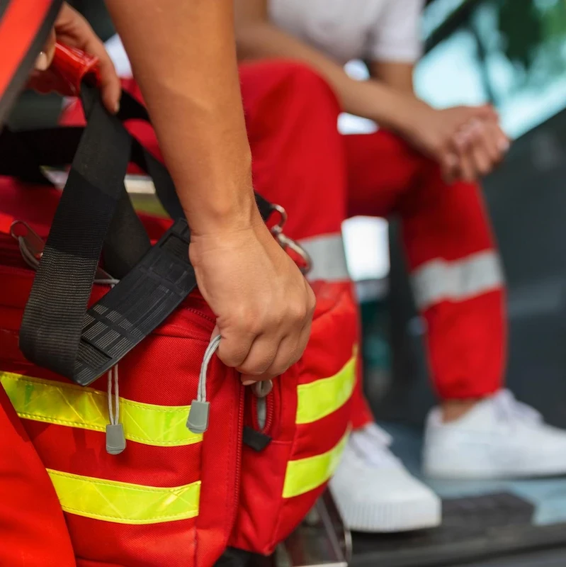 Soccorritore trasporta zaino medico rosso con bande riflettenti gialle ad alta visibilità durante intervento di emergenza.